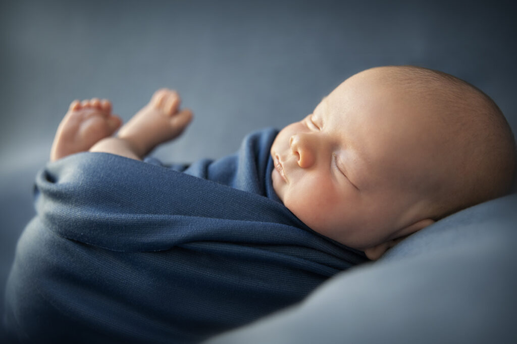 Ingebakerde baby in donkerblauwe wrap liggend op de rug op beanbag. Babyfotografie