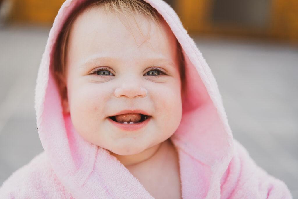 eerste levensjaar van jullie baby. De eerste stappers om te lopen. Babyfotografie. Kindje dat net kan rechtstaan en met een badjas aan, lacht naar de camera.
