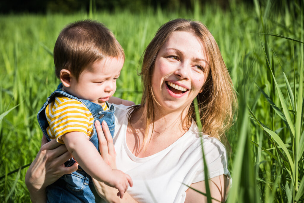 Moeder en zoon lachend in het hoge groene gras. Familie-en-portretfotografie-kinderfotografie